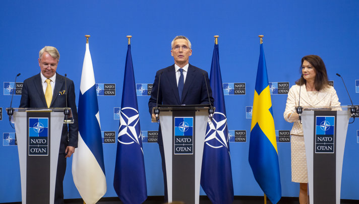Jens Stoltenberg and the foreign affairs ministers of Sweden and Finland standing on a podium.