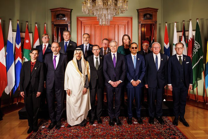 Foreign ministers from the Middle East, the Nordics and the Benelux countries standing in front of flags in a meeting room..