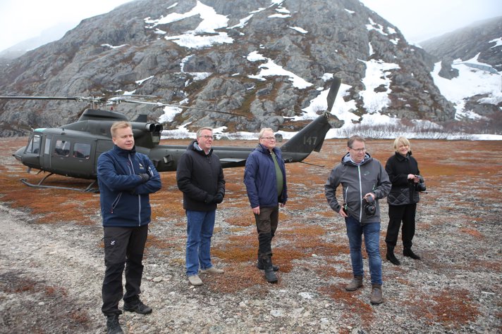 The ministers standing outside on a hilltop with a helicopter.