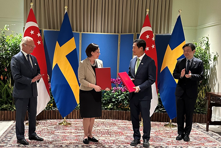 Three men and one woman standing in front of Swedish and Singaporean flags
