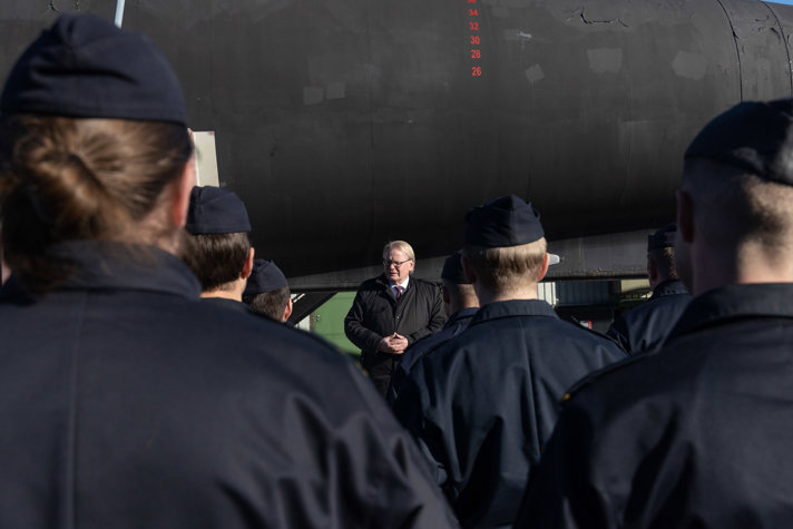 Peter Hultqvist standing outside in front of a ship talking to soldiers.