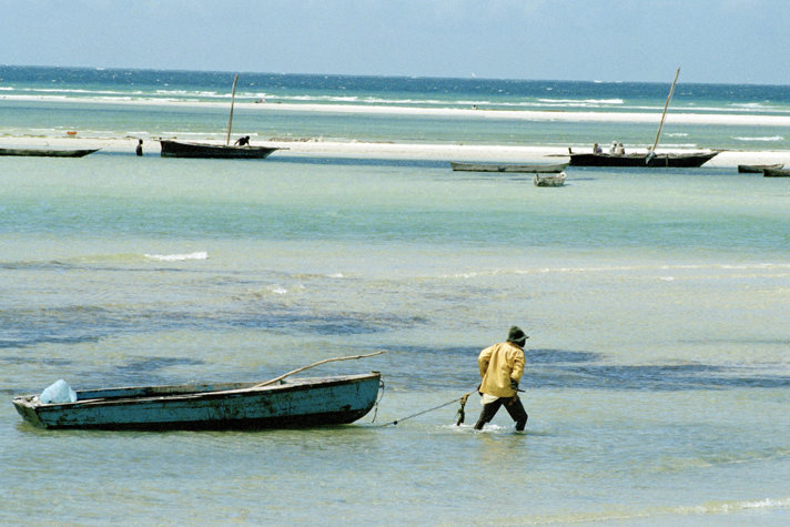 Fisherman dragging boat in shallow water