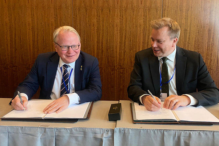 Peter Hultqvist and Antti Kaikkonen sitting next to each other and write their names on some paper.
